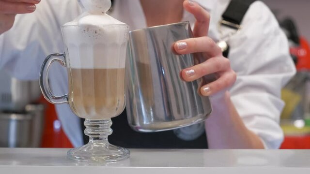 Close-up shot of a barista topping an ice-cold drink with a frothy milk mixture on the bar counter in a coffee shop. Slow motion.