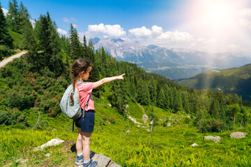Naklejka premium Children hiking on beautiful summer day in alps mountains Austria, resting on rock and admire amazing view to mountain peaks. Active family vacation leisure with kids. Outdoor fun and healthy activity