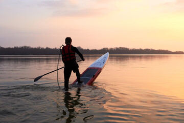 Paddle boarder. Black sunset silhouette of young sportsman paddling on stand up paddleboard....