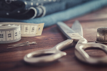 Sewing items - tailoring scissors, measuring tape, including pins, thimble. Blue jeans fabrics for sewing on background.