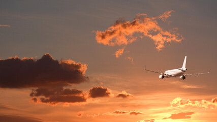 Zoom photo of modern passenger airplane flying towards sunset with cloudy sky and beautiful golden colors