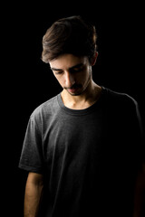 Young man portrait with a grey shirt looking down. low key photography. black background
