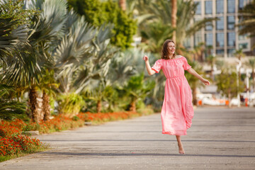 Young woman on a beach near palm trees weared in pink dress. Tropic vacation. Sea relax and rest....