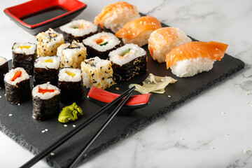 Delicious assorted sushi with chopsticks and soy sauce on a stone board.