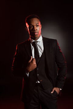 stylish african american man in formal wear standing with hand in pocket on black