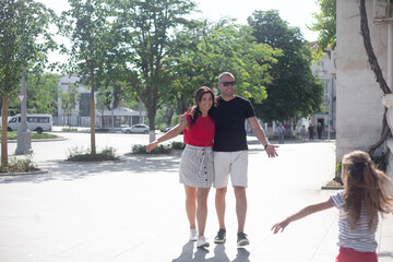 Happy family with child walking in the street of the city.  People laughing, spend time together. The kid run to hug parent