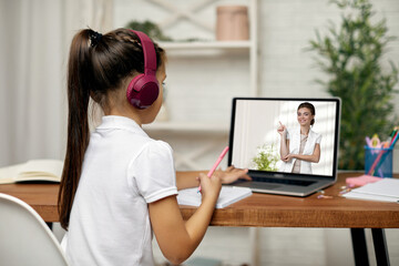 Fototapeta na wymiar little child girl in headphones have video call with teacher using laptop for studying online. online lesson at home. online video call with teacher