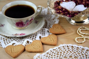 LOVE ciasteczka serca z napisem na drewnianym tle, filiżanka z kawą, płatki róż, perełki, Walentynkowe ciasteczka, vintage © Anna