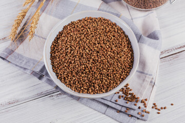 Organic uncooked scattered buckwheat grain in a bowl on a white wooden rustic background. Healthy and diet food concept.