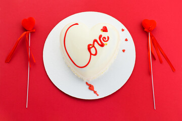 A cake in heart shape.  Mousse light cake in the shape of a heart with the inscription love with red hearts on a red background. Valentine's Day.
