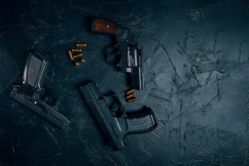 Top view of pistols and copper bullets on black concrete table. Vintage revolver with a drum. 9mm handgun. Criminal or police arsenal. Several types of dangerous firearms. Flat lay and copy space.