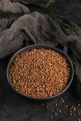 Organic uncooked scattered buckwheat grain in a bowl on a black background. Healthy and diet food concept.