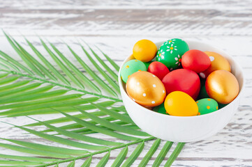 Trendy colored easter eggs, green tropical leaves and feathers on a plate on wooden table. Preparation for easter holidays. Fesstive composition