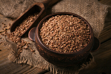 Organic uncooked scattered buckwheat grain in a bowl and wooden scoop on a rustic wooden background. Healthy and diet food concept.