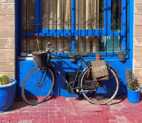 An old bicycle in front of a blue window with bars and flower pots