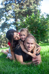 Fototapeta premium happy parents with daughter lies on the green grass. People having fun on the park. Woman and kid hug the father
