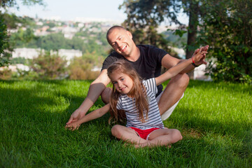 Fototapeta premium Happy family laughing in green grass of the park. Father plays with daughter. People have fun
