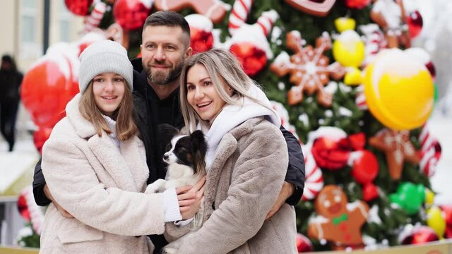 beautiful family with dog Papillon near Christmas tree on street. photo shoot