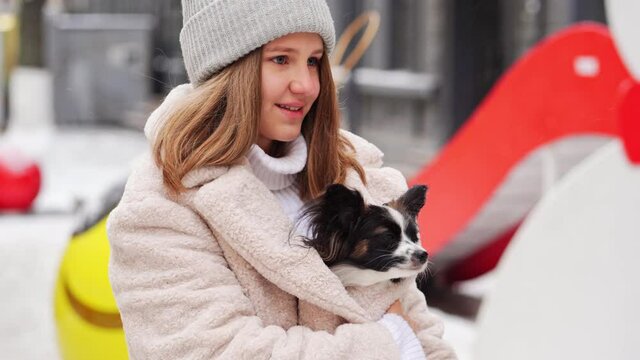 Beautiful girl with dog Papillon in her arms on winter Christmas streets