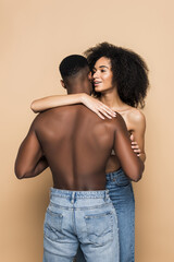 happy african american woman whispering in ear and embracing boyfriend on beige