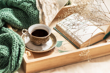 Coffee in bed, romantic morning. Flowers in a vase, an open book and a cup of coffee on a wooden tray. Home cozy interior, lifestyle. Selective focus
