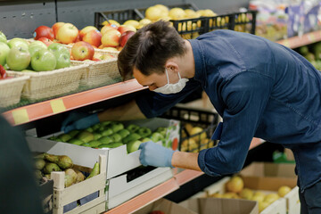 man in a protective mask standing near the counter with apples.