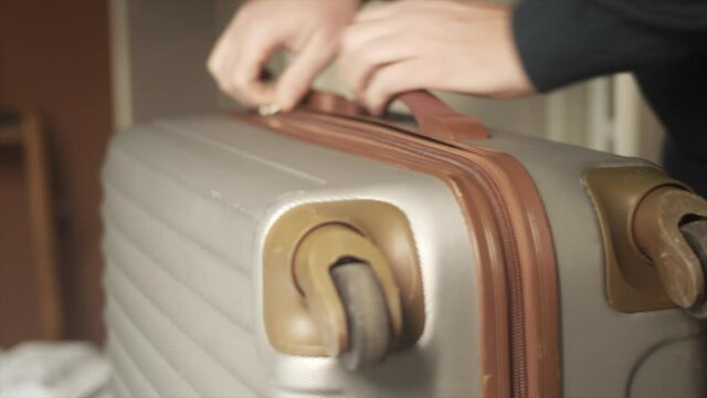 Person zips grey suitcase shut and carries out of frame, Close Up