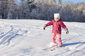 Fototapeta na wymiar 4 year old girl on cross-country skiing, no sticks. Family sports. Beautiful winter landscape.