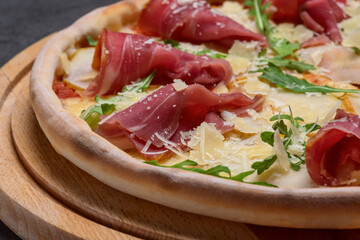 Italian pizza with sliced prosciutto ham, cheese, and fresh green rocket leaves closeup