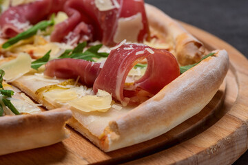 Italian pizza with sliced prosciutto ham, cheese, and fresh green rocket leaves closeup
