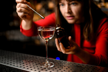 view of glass with liquid in which woman accurate adds the ingredient drop by drop