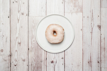 White glazed donut doughnut on a white plate on a white wooden background with copy space and room for text