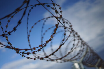 Barbed razor wire fence with rust at border or airport, migration crisis concept