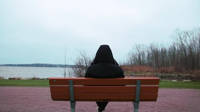 Back View Of A Man In Black Jacket Sitting Alone On A Bench Facing The Baltic Sea In Finland - zoom-in