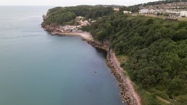 Aerial circling shot of stony famous Babbacombe Beach with green cliffs and Torquay Town on top of mountain.