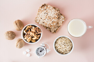 Good sleep. Foods for good sleep - milk, walnuts, crispbread, oatmeal, sleeping pill and alarm clock on pink background. Top view