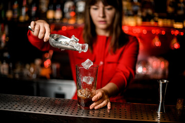 woman's hand holds scoop with ice cubes and carefully pours them into glass with drink