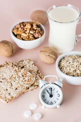 Good sleep. Foods for good sleep - milk, walnuts, crispbread, oatmeal, sleeping pill and alarm clock on pink background. Vertical view