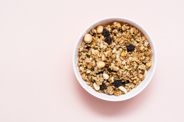 Fototapeta na wymiar Healthy eating. Baked oats, nuts and raisins granola in a bowl on a pink background. Top view