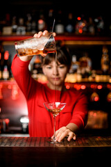 wineglass stands on bar and bartender holds mixing cup and skilfully pours drink into it