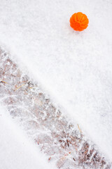a bright orange ball lies on the snow-white snow next to the track from the car wheel