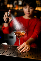 glass with cocktail stands on bar counter and female bartender accurate sprinkles on it