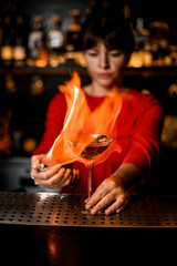 female barkeeper holds glass on bar counter and sets it on fire