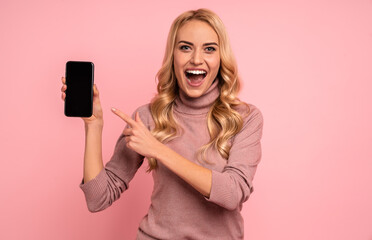 Portrait of an excited young woman showing blank screen mobile phone isolated over pink background