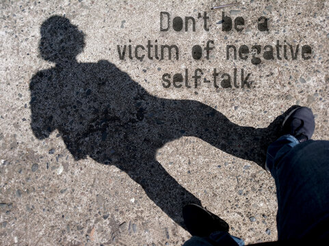 Inspirational motivational quote  - Do not be a victim of negative self talk. On background of silhouette shadow of a person walking on the street.