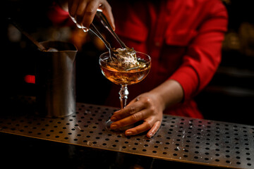 woman's hand holding tongs with ice cube and put it into glass of drink
