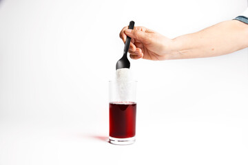 Hand pouring some additives, sugar, white powder, preservatives into a glass of healthy drink with a black spoon.