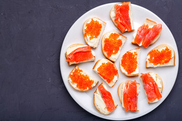 Bruschettes with butter and red caviar and salmon on a white plate on a gray concrete background copy space.