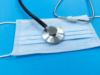 Black stethoscope on disposable face mask on blue background. Medical concept.