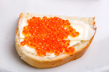 Bruschetta with butter and red caviar on a white plate close-up.